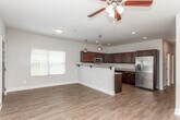 Located at 1805 Shiloh Rd NW in Kennesaw, Georgia, this two-story home offers a thoughtfully designed layout across two levels. The main floor welcomes you through a bold dark front door with a glass accent panel, opening into a bright, open living area bathed in natural light from multiple windows dressed with white blinds. Rich wood-look flooring extends throughout the main level, creating a warm and cohesive aesthetic. The kitchen is a standout feature, showcasing deep espresso-toned cabinetry, granite countertops, stainless steel appliances including a range, microwave, and dishwasher, and warm pendant lighting — all centered around a generous U-shaped layout ideal for cooking and entertaining. A convenient half bath on the main floor features dark cabinetry with a granite vanity top and wood-look flooring. Upstairs, the bedrooms are finished with plush carpeting, ceiling fans, and dark five-panel doors that add a modern touch. The upper-level bathrooms are well-appointed with dark vanities, granite countertops, and tub-shower combinations. A staircase with decorative iron railings connects both floors, adding an architectural detail visible from the open-concept dollhouse view of the home.