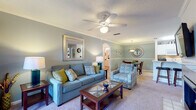 This single-story, 2-bedroom, 2-bathroom residence is thoughtfully designed with a cohesive color palette of soft blue-gray tones, neutral carpeting, and warm wood-look flooring that carries throughout key areas. The living room serves as the central gathering space, featuring crown molding, a ceiling fan, and a framed mirror accent wall. French doors open to an outdoor area, filling the room with natural light. The space flows seamlessly into a dedicated dining area, distinguished by chair-rail molding, decorative wall art, and a stylish sunburst mirror.

The galley-style kitchen is efficiently laid out with white cabinetry, white appliances, and warm hardwood-style flooring that maximizes functionality. Both bedrooms are generously sized with plush carpeting, ceiling fans, and multiple windows providing ample natural light. One bedroom features a walk-in closet with built-in shelving, while the other includes multiple windows on two walls. The bathrooms are finished with white vanity cabinetry, large mirrors, and hardwood-style flooring. The floorplan model reveals a well-organized layout that balances open communal spaces with private retreats.