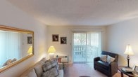 This single-floor residence at 2233 W Jefferson St in Kokomo, Indiana offers a practical and comfortable layout across several well-defined living spaces. The living room serves as the heart of the unit, featuring soft carpeting, a textured ceiling, and a large sliding glass door fitted with vertical blinds that opens to an outdoor patio, allowing natural light to fill the room and providing views of surrounding greenery. A gold-framed mirror and framed wall art add decorative character to the space.

The kitchen is efficiently designed with ample white cabinetry extending to the ceiling for generous storage. It includes a double-basin sink, electric range, dishwasher, and a full-size refrigerator. A skylight-style overhead fixture brightens the workspace, and light-toned countertops complement the clean, white aesthetic throughout.

The bedroom is a well-proportioned retreat with plush carpet, a textured ceiling, and a window dressed with dark curtains that offer privacy while admitting natural light. The room comfortably accommodates a full bedroom suite.

The bathroom features tile flooring, a tub-shower combination with a decorative curtain, and neutral wall tones that create a clean, functional environment. Overall, the unit offers a cohesive, move-in-ready atmosphere suitable for comfortable everyday living.
