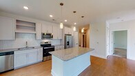 Located at 305 Oberlin Rd in Raleigh, NC, this well-appointed single-floor residence offers a thoughtfully designed open-concept layout with modern finishes throughout. The kitchen serves as the heart of the home, showcasing crisp white shaker cabinetry, a herringbone-patterned tile backsplash, granite countertops, and a central island with built-in shelving — all illuminated by elegant pendant lighting. Stainless steel appliances, including a side-by-side refrigerator with ice dispenser, electric range, over-the-range microwave, and dishwasher, complete the space. Large windows flood the kitchen and adjacent living area with natural light and offer lush, tree-lined views, creating a bright and inviting atmosphere. The spacious living area features warm hardwood-style flooring and a ceiling fan, while large multi-pane windows frame greenery views on two sides. Bedrooms are carpeted for comfort, each equipped with ceiling fans, generous closet space — including walk-in configurations — and windows overlooking the surrounding tree canopy. The bathrooms are finished with granite-topped vanities, white shaker cabinetry, and classic white tile surrounds. A convenient half bath provides additional functionality. Throughout the unit, clean lines, neutral tones, and quality materials contribute to a cohesive, modern aesthetic.