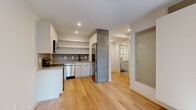 Located at 2009 North Howard Street in Philadelphia's vibrant 19122 corridor, this thoughtfully designed one-bedroom, one-bathroom unit offers a modern and efficient living experience across a single floor. Light hardwood flooring runs throughout, tying the space together with a warm, cohesive aesthetic.

The kitchen is well-appointed with white shaker-style cabinetry extending to the ceiling, stainless steel appliances including a range, microwave, and dishwasher, complemented by a textured tile backsplash and a black matte sink fixture. Open shelving adds both function and style.

The living room is bright and airy, benefiting from multiple windows and a glass door that invite natural light and provide views of the surrounding neighborhood. A ceiling fan adds comfort to the space.

The bedroom is a calm retreat featuring a built-in closet with clean panel doors, a transom window above for additional light, and a standard window with a roller shade. The room is serene and functional.

The bathroom features large-format grey tile flooring, a sleek floating vanity with an illuminated mirror, and a clean, minimalist design. A frosted glass door adds a modern touch while maintaining privacy.

A connecting hallway with a frosted glass sliding door completes this clean, contemporary layout.