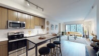 Located in the heart of Cincinnati at 401 Race St, this single-floor residence combines contemporary design with functional living spaces. The open-concept layout connects the kitchen and living area seamlessly, creating a bright, cohesive environment anchored by large floor-to-ceiling windows that frame views of the surrounding downtown cityscape.

The kitchen is well-appointed with warm wood-toned cabinetry, white quartz countertops, a white subway tile backsplash, and a full suite of stainless steel appliances. A spacious island with bar seating serves as both a prep area and casual dining space. Light wood-style flooring runs throughout the main living areas, complementing the neutral color palette.

The living room offers generous proportions, benefiting from abundant natural light pouring in through large sliding windows with direct city views. The space accommodates comfortable furnishing arrangements and features clean, modern wall finishes.

The primary bedroom includes large windows with urban views and plush carpeting, while a second bedroom provides a quieter, cozily scaled retreat. Two bathrooms are finished with dual-sink wood vanities, white quartz countertops, and wood-look tile flooring. One features a soaking tub with tiled surround, and the other offers a double vanity with a clean, minimalist aesthetic throughout.