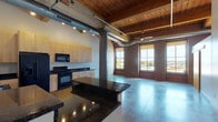 Located in St. Louis, MO, this single-floor loft showcases a compelling blend of industrial character and modern finishes. The open-plan living and kitchen area is anchored by polished concrete floors, soaring wood-beamed ceilings with exposed timber, and original brick accent walls that lend authentic urban charm. Large windows allow generous natural light to flood the space while offering city views, complemented by ceiling fans and track lighting throughout.

The kitchen is well-appointed with light maple cabinetry, dark granite countertops, a central island, and black appliances including a refrigerator, range, microwave, and dishwasher. A dedicated laundry area is accessible off the kitchen. Exposed ductwork and structural steel columns add to the loft's industrial aesthetic.

A corridor with warm wood-plank ceilings and track lighting connects the main living area to the private spaces. Two bathrooms are present: one features a sleek, modern vanity with a glass sink and a tiled walk-in shower, while the second offers a full soaking tub and polished concrete floors. Additional rooms provide flexible space for bedrooms or offices, each featuring the signature concrete floors, exposed columns, and wood ceilings that define the overall aesthetic of this distinctive St. Louis loft.