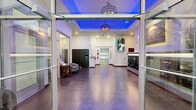 Located at 2723 California Ave SW in Seattle's West Seattle neighborhood, Admiral Station's ground-floor lobby presents a well-appointed communal space designed to serve residents with both functionality and visual appeal. The generously sized single-floor layout accommodates several distinct functional areas that flow seamlessly into one another.

The main lobby entrance features large glass double doors that flood the interior with natural light, opening into a polished concrete-floored reception area. A signature architectural detail is the raised tray ceiling, illuminated with vibrant blue ambient lighting and anchored by stylish industrial-style pendant fixtures, creating a striking focal point overhead. White walls adorned with nautical-themed artwork and motivational decor reinforce the building's Admiral Station identity.

Resident mailboxes—both traditional and smart parcel lockers—line the walls, providing convenient mail retrieval. A staffed management office with glass partitions sits adjacent to the lobby, accompanied by a small seating area. A stainless steel elevator offers access to upper floors. A dedicated fitness room with glass doors and teal accent walls houses exercise equipment. A utility corridor with office storage and service cart access completes the functional back-of-house areas.