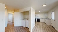 Located at 2272 W 10th Ave in Junction City, Oregon, this single-floor unit offers a clean, modern layout designed for comfortable everyday living. The kitchen is a standout feature, equipped with white cabinetry, granite-style countertops, and black appliances including a range, dishwasher, and refrigerator. Light vinyl plank flooring runs throughout the kitchen and main living areas, providing a bright, easy-to-maintain surface. Natural light enters through multiple windows fitted with blinds, offering views of the surrounding neighborhood and open landscape. A dedicated in-unit laundry alcove houses a full-size washer and dryer, adding convenience to daily routines. The living and dining areas are open and well-lit, with a wall-mounted HVAC unit providing climate control. The bedrooms are carpeted for warmth and comfort, each featuring a window that allows in natural light. The bathrooms include one full bath with a tub-shower combination and a second bathroom with a walk-in shower stall, white vanity with granite-style countertops, and wood-look vinyl flooring. The overall design is neutral and contemporary, with cream-toned walls and consistent finishes throughout.