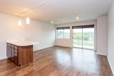 This single-floor unit is designed with a clean, contemporary aesthetic that carries consistently throughout each space. Rich, dark hardwood-style flooring anchors the interior, complementing the neutral gray-toned walls and white baseboards found in every room.

The open living area is generously proportioned, bathed in natural light from a large sliding glass door that leads to a private balcony overlooking a green, tree-lined exterior. Track lighting runs along the ceiling, providing flexible, adjustable illumination across the space.

The kitchen is well-appointed and functional, featuring rich dark-wood cabinetry, marble-patterned countertops, and a full suite of stainless steel appliances including a refrigerator, range, microwave, and dishwasher. A kitchen island with matching cabinetry and countertop surface provides additional prep space and serves as a natural divider between the kitchen and living areas. Pendant lighting above the island adds a refined finishing touch.

A separate bedroom offers a quieter retreat, continuing the same flooring and neutral wall palette, with track lighting overhead. The bathroom is efficiently laid out with a marble-finish vanity countertop, dark wood cabinetry with overhead storage, a large mirror, and a tub-shower combination with a frosted glass door.