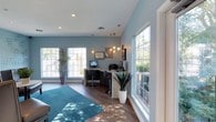 The community space at Enclave at Huntington Woods is a thoughtfully designed single-floor area that blends functionality with contemporary style. The room is characterized by soft blue-gray walls that create a calm, inviting atmosphere, complemented by rich hardwood flooring and a vibrant teal area rug that adds a pop of color to the space.

Natural light fills the room through multiple large windows framed in white trim, offering views of lush greenery outside and creating a bright, airy environment throughout the day. Recessed ceiling lighting works alongside a striking cluster of globe pendant lights to ensure the space remains well-lit and visually appealing.

A dedicated business center occupies one corner of the room, featuring sleek workstations with computers and office equipment, supported by modern bar-height seating. Decorative wall art and carefully placed tropical potted plants add warmth and personality to the space.

Overall, the room strikes a balance between a professional and comfortable setting, making it a versatile communal area well-suited for both productivity and relaxation.