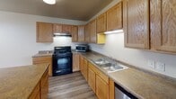 Located at 3403 11th St SE in Minot, North Dakota, this single-floor unit offers a practical and well-organized layout designed for comfortable everyday living. The kitchen is a standout feature, equipped with warm oak cabinetry that extends to the upper walls, providing generous storage throughout. Dark countertops offer ample workspace, and the kitchen includes a black gas range, a double stainless steel sink, a dishwasher, and a refrigerator. Light wood-style flooring runs throughout the kitchen, complementing the cabinetry. A peninsula adds additional counter space and helps define the kitchen area within the open layout.

The living area features neutral carpet and light-toned walls, creating a calm and versatile space. A large window allows natural light to fill the room while offering views of the surrounding green landscape and neighboring buildings.

The bathroom is thoughtfully designed with accessibility in mind, featuring stainless steel grab bars near the tub-shower combination and toilet, tile flooring, an oak vanity with a granite-style countertop, and a solid wood door. The dedicated laundry area includes side-by-side full-sized front-loading washer and dryer units with overhead shelving, providing added in-unit convenience.