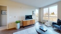 This 590 square foot apartment in Seattle combines modern design with efficient use of space. The open-concept living area is flooded with natural light from large windows, offering picturesque views of the surrounding landscape. The contemporary kitchen boasts sleek cabinetry, stainless steel appliances, and a practical layout with a breakfast bar, perfect for casual dining or entertaining.

The 130 square foot bedroom features a large window, providing ample natural light and views. It's complemented by a closet for storage. The bathroom is well-appointed with a modern vanity, toilet, and a washer and dryer for convenience.

Throughout the apartment, the design aesthetic is cohesive, with a neutral color palette accented by pops of blue in the decor. The living room showcases a comfortable seating area with a stylish sofa, armchair, and coffee table, creating an inviting space for relaxation. Hardwood-style flooring runs throughout, adding warmth and durability.

Thoughtful touches like contemporary light fixtures, carefully chosen artwork, and strategically placed plants enhance the overall ambiance. Despite its compact size, this apartment offers a harmonious blend of style, functionality, and comfort, making efficient use of every square foot.