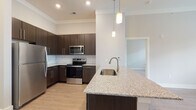 This single-floor residence offers a thoughtfully designed layout with modern finishes throughout. The kitchen serves as a central highlight, featuring dark espresso cabinetry that extends to the ceiling, a classic white subway tile backsplash, and a full suite of stainless steel appliances including a refrigerator, range, and over-the-range microwave. A peninsula island with a granite countertop and undermount sink provides additional prep space and is accented by stylish pendant lighting above. Light wood-look flooring flows throughout the main living and kitchen areas, lending warmth and cohesion to the space.

The bedrooms are carpeted for comfort and feature tall ceilings that enhance the sense of openness. One bedroom includes access to an adjoining space, likely a closet or laundry area, and benefits from a large window that brings in natural light and exterior views.

Two bathrooms round out the residence. The primary bathroom features a dark espresso vanity with a granite-topped sink, a framed mirror, and light wood-look flooring. The second bathroom is finished with a clean white tub-shower combination, brushed nickel fixtures, and a bright, neutral palette. Together, the spaces reflect a cohesive, contemporary aesthetic suited for comfortable everyday living.