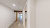 Located at 230 Goldsboro St S in Wilson, NC, this 1-bedroom, 1-bathroom unit masterfully blends industrial character with modern finishes. Polished concrete floors run throughout the entire space, complemented by striking exposed wood beams that trace the length of the hallways and living areas, adding warmth and a sense of history to the clean, white-painted interior.

The open kitchen and living area serves as the heart of the unit, featuring a peninsula with a built-in sink and light quartz countertops, gray shaker cabinetry, and a full suite of stainless steel appliances including a refrigerator, range, and microwave. The living area benefits from natural light streaming through windows framed by an original exposed brick wall, creating a compelling industrial-chic focal point.

The hallway connects the main living spaces to the bedroom, bathroom, and utility room. The bedroom is a well-proportioned, quiet retreat, featuring an overhead exposed beam. The bathroom is cleanly appointed with a tub-shower combo, a vanity with white countertop, and classic penny tile flooring. A dedicated utility room and ample hallway space round out this thoughtfully designed, character-rich unit.