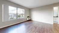 Located on Emelita Street in the Valley Village neighborhood of Los Angeles, this 1-bedroom, 2-bathroom unit offers a well-designed, functional layout across a single floor. The open-concept living and kitchen area is bright and welcoming, anchored by warm hardwood-style flooring and a ceiling fan overhead. A large window fills the living space with natural light while offering views of the surrounding neighborhood, including palm trees characteristic of the LA landscape. The kitchen is efficiently designed in a galley style, featuring white shaker cabinetry, dark countertops, stainless steel appliances including a gas range, microwave, and refrigerator, a skylight for added brightness, and a peninsula with a sink that opens to the living area. The bedroom is carpeted for comfort and includes a window overlooking the neighborhood, and connects to a dedicated walk-in closet outfitted with built-in shelving, hanging rods, and ample storage space. Two full bathrooms serve the unit, one of which includes a tub/shower combination with clean white finishes. The unit's neutral color palette, clean lines, and practical layout create a comfortable and modern living environment well-suited for everyday life in Los Angeles.
