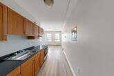 This thoughtfully laid-out studio unit makes excellent use of its compact footprint across a single floor, encompassing a combined kitchen and living area, a full bathroom, and a dedicated closet. The open-plan kitchen and living space forms the heart of the unit, where warm medium-toned wood cabinetry lines one wall, offering ample upper and lower storage. The kitchen is equipped with dark countertops, a stainless steel double sink, and a stainless steel range, providing all the essentials for everyday cooking. Light hardwood-style flooring extends throughout, lending a clean, cohesive aesthetic. The living area benefits from multiple windows that invite natural light and offer views of the surrounding neighborhood, creating a bright and airy atmosphere despite the unit's compact scale. Baseboard heating runs along the perimeter, ensuring comfort year-round. A sliding-door closet provides convenient storage within the living space. The bathroom features classic beige ceramic tile flooring, a white vanity with a mirrored medicine cabinet, and a full tub-shower combination — all finished in a neutral palette that contributes to a clean, functional design. Track lighting and flush-mount ceiling fixtures provide additional illumination throughout the unit.
