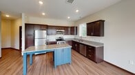 Located at 3000 N Chestnut St in Chaska, Minnesota, this single-floor unit offers a well-designed layout with thoughtfully selected finishes throughout. The kitchen serves as a central highlight, featuring rich dark-stained cabinetry, granite countertops, stainless steel appliances including a refrigerator, range, microwave, and dishwasher, and a distinctive blue-accented center island that provides additional prep space and casual seating. Light wood-look flooring runs through the kitchen and living areas, contributing to a clean, cohesive aesthetic.

The open-concept living area is bright and airy, benefiting from multiple windows and a sliding glass door that opens onto a private balcony with outdoor views. Natural light flows generously through the space, enhancing its welcoming atmosphere.

The bedrooms are carpeted for comfort and each feature ceiling fans, windows with natural light, and closet space. One bedroom includes a walk-in closet with built-in shelving.

The bathrooms are finished consistently with granite-topped dark vanities and wood-look flooring. One bathroom includes a tub-shower combination, while another features a longer vanity layout with additional storage, reflecting a practical and polished design throughout the unit.