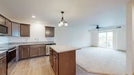 Located at 1690 Premier Dr in Mankato, MN, this well-appointed one-bedroom, one-bathroom unit offers a thoughtfully designed single-floor layout. The open-concept kitchen and living area serves as the heart of the home, where rich dark-stained cabinetry, granite countertops, and a central island with pendant lighting create a functional and stylish space. Stainless steel appliances — including a refrigerator, range, microwave, and dishwasher — complete the kitchen. Light hardwood-style flooring flows throughout the kitchen and main areas, transitioning to plush carpet in the living room and bedroom. The living room is bright and airy, featuring a ceiling fan and sliding glass doors that open to a private balcony with outdoor views. The generously sized primary bedroom offers ample natural light, soft carpeting, and a closet with built-in shelving. The bathroom mirrors the home's design aesthetic with a granite-topped vanity, dark wood cabinetry, and a well-lit mirror. A dedicated in-unit laundry room with a full-size washer and dryer adds everyday convenience. Throughout the space, warm neutral tones and consistent finishes lend a cohesive, modern feel.