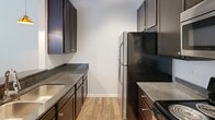 Located at 1415 Chambers Ave, this single-floor, one-bedroom, one-bathroom residence offers a thoughtfully arranged layout that maximizes functionality throughout. The kitchen features dark espresso cabinetry paired with granite-style countertops, wood-look tile flooring, and stainless steel appliances including a full-size refrigerator. A kitchen peninsula with a double undermount sink and pendant lighting provides a natural transition into the living area, which is illuminated by natural light streaming through multiple windows fitted with horizontal blinds. The living space is anchored by a ceiling fan overhead, contributing to a bright and airy atmosphere. The bedroom is carpeted for comfort and includes a ceiling fan with a light fixture, a window for natural light, and direct access to a dedicated closet for ample storage. The bathroom is clean and efficiently designed, featuring tile flooring, a tub-shower combination, a dark-cabinetry vanity with a granite-style countertop, an undermount sink, and wall sconce lighting. Throughout the residence, crisp white walls and consistent finishes create a cohesive and welcoming ambiance, making this a practical and comfortable single-level home.