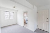 This single-floor unit offers a practical and well-organized layout, as revealed by the floor plan, which comprises a spacious living area, multiple bedrooms, a kitchen, and a full bathroom. The living area is generously proportioned, featuring neutral-toned carpet flooring, cream-painted walls, and grid-pane windows that allow natural light to filter in alongside views of surrounding trees. A central entry door with brass hardware provides direct access to the main living space.

The kitchen is efficiently designed with light wood cabinetry offering ample upper and lower storage, white laminate countertops, a stainless steel sink positioned beneath a window, tile flooring, and a white electric range with a ventilation hood overhead. The space opens conveniently toward the dining or living area.

The bedrooms are carpeted and share a consistent aesthetic of neutral walls and grid-pane windows. Several rooms include standard closets with bifold doors, and ceiling-mounted light fixtures with brass accents are present throughout.

The bathroom features a classic design highlighted by white subway tile walls accented with black borders, a black-and-white mosaic tile floor, a white vanity, toilet, and bathtub, along with a window providing natural ventilation.