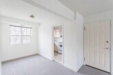 This single-floor unit offers a practical and well-organized layout, as revealed by the floor plan, which comprises a spacious living area, multiple bedrooms, a kitchen, and a full bathroom. The living area is generously proportioned, featuring neutral-toned carpet flooring, cream-painted walls, and grid-pane windows that allow natural light to filter in alongside views of surrounding trees. A central entry door with brass hardware provides direct access to the main living space.

The kitchen is efficiently designed with light wood cabinetry offering ample upper and lower storage, white laminate countertops, a stainless steel sink positioned beneath a window, tile flooring, and a white electric range with a ventilation hood overhead. The space opens conveniently toward the dining or living area.

The bedrooms are carpeted and share a consistent aesthetic of neutral walls and grid-pane windows. Several rooms include standard closets with bifold doors, and ceiling-mounted light fixtures with brass accents are present throughout.

The bathroom features a classic design highlighted by white subway tile walls accented with black borders, a black-and-white mosaic tile floor, a white vanity, toilet, and bathtub, along with a window providing natural ventilation.
