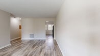 This compact yet efficiently designed single-floor residence offers a thoughtfully organized layout comprising a living room, bedroom, kitchen, bathroom, and hallway. The interior is unified by light-toned wood-look flooring that flows through the main living areas, complemented by crisp white trim and neutral beige walls that create a clean, airy atmosphere throughout.

The living room is a bright, open space featuring a large window that draws in natural light, a front entry door, and a floor vent for climate control. It connects seamlessly to the rest of the home via a hallway. A secondary living area transitions into the kitchen, which is outfitted with white cabinetry, black appliances including an electric range, microwave, and dishwasher, a stainless steel sink, and dual windows that bathe the space in natural light.

The bedroom is a generously sized retreat with soft wall-to-wall carpeting, a ceiling fan with light fixture, a window with blinds, and two doors — one leading to the hallway and one to a closet — offering ample storage. The bathroom is finished in all-white tile surrounding a full bathtub and shower combination, accented by a window with blinds for ventilation and natural light. The overall ambiance is clean, neutral, and move-in ready.