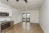 This single-floor unit showcases a clean, contemporary design throughout its open-concept layout. Light hardwood flooring extends across the main living area, creating a bright and cohesive aesthetic that complements the crisp white walls and modern finishes.

The kitchen is efficiently designed with two-tone cabinetry—combining white upper cabinets with warm wood-grain lower cabinets—and is equipped with a full suite of stainless steel appliances, including a refrigerator, electric range, built-in microwave, and dishwasher. A white quartz countertop and subway tile backsplash add a polished, contemporary touch. Track lighting above the kitchen and a ceiling fan over the living area provide both functional illumination and airflow.

A dedicated in-unit laundry closet houses a stacked washer and dryer, offering added convenience. The bathroom features a wood-toned vanity with a white quartz countertop and a glass-enclosed walk-in shower with large-format gray tile, lending a spa-like quality to the space.

The living area is generously proportioned and benefits from large windows that frame city views, filling the space with natural light. The overall ambiance is contemporary, clean, and move-in ready.