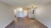 Located at 563 Deere Park Circle in Bartlett, Illinois, this single-floor unit offers a straightforward, functional layout spread across several distinct spaces. The main living area is generously proportioned, featuring warm wood-style laminate flooring, neutral gray walls, and a ceiling fan with integrated lighting. A large window at the far end of the living room fills the space with natural light and offers a view of the surrounding greenery, while a wall-mounted air conditioning unit and baseboard heating provide year-round climate control.

The kitchen is efficiently designed, showcasing gray-toned cabinetry with a stainless steel sink, white tile backsplash, and black appliances including a gas range and refrigerator. Adjacent to the living area, a dedicated hallway leads to the bedroom, which is finished with plush carpeting and includes a built-in closet with upper storage cabinetry, offering practical organization. The bathroom features a full tub and shower combination with white tile surround, a vanity with mirror, and clean, neutral finishes throughout. The entry area provides a welcoming transition into the unit, completing this well-organized and move-in-ready space.