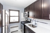 Located at 409 Church St in Hasbrouck Heights, NJ, this single-floor unit presents a cohesive and well-maintained interior with a consistent design language throughout. The space is unified by rich, warm-toned hardwood flooring that flows seamlessly from room to room, complemented by cool blue-gray walls and crisp white baseboards and trim.

The living and dining areas are open and functional, benefiting from natural light admitted through dark-framed windows that offer views of the surrounding neighborhood. Baseboard radiators provide efficient heating in multiple rooms. Recessed lighting in select areas adds a modern touch to the overall aesthetic.

The kitchen stands out as a clearly updated space, featuring dark espresso-toned cabinetry, light quartz countertops, a subway tile backsplash with a decorative mosaic accent strip, stainless steel appliances including a gas range and dishwasher, and a chrome faucet over a stainless steel sink.

The bathroom continues the tile motif with full subway tile surrounding a soaking tub and shower, accented by a matching mosaic border. Wood-look tile flooring and a natural light source via a window complete the clean, bright aesthetic. The bedrooms are generously proportioned, quiet, and filled with natural light.
