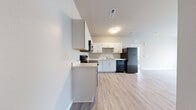 Located at 1300 Lancaster Rd in South Elgin, IL, this 560-square-foot, one-bedroom, one-bathroom apartment offers a clean and modern design throughout its single-floor layout. The kitchen is outfitted with crisp white cabinetry featuring brushed-nickel hardware, light countertops, and black appliances including a range with over-the-range microwave, dishwasher, and refrigerator. Light wood-look flooring runs through the kitchen and living areas, creating a cohesive and easy-to-maintain aesthetic. The 130-square-foot bedroom features plush carpeting, a ceiling fan with a gold-toned light fixture, and a large multi-panel window dressed with horizontal blinds that allows ample natural light. The bedroom also provides direct access to both the bathroom and an additional room. The bathroom is well-appointed with white cabinetry, a single-sink vanity, wood-look flooring, and a full tub/shower combination with a curved curtain rod. A dedicated laundry room offers added convenience with an in-unit top-load washer and dryer, wire shelving for storage, and a water heater. The unit's neutral color palette and modern finishes create a clean, functional living environment suited for everyday comfort.