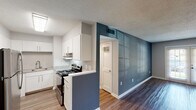 Located at 221 N Graham Hopedale Rd in Burlington, NC, this single-floor residence offers a well-designed layout with contemporary finishes throughout. The open living area is finished with durable wood-look flooring and neutral gray walls, creating a bright and welcoming atmosphere. A panel door and window allow natural light to fill the space, enhancing its open feel.

The kitchen is a standout feature, outfitted with crisp white shaker cabinetry, granite-look countertops, subway tile backsplash, and stainless steel appliances including a refrigerator and electric range with an overhead exhaust hood. A bold teal accent wall adds a distinctive design element where the kitchen transitions into the living space.

The bedrooms are finished with plush carpet flooring and neutral tones, providing a comfortable and quiet retreat. Ceiling fans with light fixtures add functionality, while windows invite natural light. Generously sized closets with full-width hanging rods offer ample storage.

The bathroom features a clean white tub and shower surround, a granite-topped vanity with an integrated sink, a framed mirror, and brushed gold hardware accents. Textured ceilings are consistent throughout the unit, adding a classic touch to the overall design.