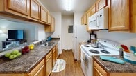 Located at 608 Wallen Hills Dr in Fort Wayne, Indiana, this single-floor residence offers a well-organized and comfortable layout designed for practical everyday living. The galley-style kitchen is efficiently arranged with light wood cabinetry lining both sides, dark laminate countertops, durable wood-look flooring, and a full suite of white appliances including a refrigerator, electric range, microwave, and dishwasher — providing ample storage and workspace for cooking. The living room is bright and inviting, featuring plush carpeting and a large sliding glass door that fills the space with natural light and offers direct views of the outdoor greenery. The primary bedroom is a restful retreat with soft carpet, warm neutral walls, and a window dressed with floor-length curtains that allow for natural light while maintaining privacy. A second bedroom, currently configured as a home office, offers carpeted flooring and a window with natural light, making it a versatile space suitable for various needs. The bathroom is well-appointed with a vanity featuring a single-sink, a wood-framed mirror, and a tub-shower combination. Throughout the residence, neutral tones, consistent flooring choices, and thoughtful layout create a cohesive and welcoming ambiance.