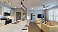 This thoughtfully designed single-floor residence in North Little Rock, AR offers a seamless blend of modern aesthetics and functional living. The open-concept layout connects the kitchen, dining, and living areas, creating an inviting and cohesive flow throughout the main living space. The kitchen is a standout, featuring stainless steel appliances, white shaker-style cabinetry with glass-front upper cabinets, a large quartz waterfall island with an undermount sink, pendant lighting, and track lighting overhead. Dark lower cabinetry on the opposite wall adds a striking contrast. The dining area is illuminated by a bold geometric chandelier and benefits from natural light through a front-facing window. The living room offers vaulted ceilings, large windows with exterior views, recessed lighting, and a ceiling fan. Bedrooms are carpeted and well-lit with natural light from oversized windows and ceiling fans. The bathrooms are elegantly finished with marble-look porcelain tile on floors and walls, a glass-enclosed walk-in shower, a soaking tub with sliding glass doors, and a wide double-vanity. A walk-in closet with built-in shelving is accessible from one of the bathrooms. Cool gray walls and warm wood-look flooring in the main areas tie the entire space together with a cohesive, contemporary palette.