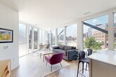 Located at 501 North Christopher Columbus Boulevard in Philadelphia's vibrant Northern Liberties neighborhood, this thoughtfully designed three-bedroom, two-bathroom residence offers a seamless blend of modern architecture and functional living. The open-concept kitchen and living area serves as the heart of the home, anchored by dramatic floor-to-ceiling windows that flood the space with natural light and frame sweeping views of the Philadelphia skyline, surrounding greenery, and the nearby waterfront. The kitchen features two-tone cabinetry in warm wood and cool gray tones, stainless steel appliances, a white subway tile backsplash, and a peninsula with bar seating — ideal for casual dining or entertaining. Light hardwood flooring flows throughout the main living areas, enhancing the bright, airy atmosphere. The generously sized primary bedroom boasts wall-to-wall windows with serene views of the tree-lined boulevard and river beyond, plush carpeting, and access to a well-appointed en-suite bathroom with a glass-enclosed marble-tiled shower. The second bathroom features a double vanity with a wood-framed mirror and a marble-tiled tub-shower combo. Each bedroom offers ample closet space, including walk-in closets with multi-tier wire shelving systems. The hallway is clean and well-lit, completing this polished urban residence.