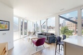 Located at 501 North Christopher Columbus Boulevard in Philadelphia's vibrant Northern Liberties neighborhood, this thoughtfully designed three-bedroom, two-bathroom residence offers a seamless blend of modern architecture and functional living. The open-concept kitchen and living area serves as the heart of the home, anchored by dramatic floor-to-ceiling windows that flood the space with natural light and frame sweeping views of the Philadelphia skyline, surrounding greenery, and the nearby waterfront. The kitchen features two-tone cabinetry in warm wood and cool gray tones, stainless steel appliances, a white subway tile backsplash, and a peninsula with bar seating — ideal for casual dining or entertaining. Light hardwood flooring flows throughout the main living areas, enhancing the bright, airy atmosphere. The generously sized primary bedroom boasts wall-to-wall windows with serene views of the tree-lined boulevard and river beyond, plush carpeting, and access to a well-appointed en-suite bathroom with a glass-enclosed marble-tiled shower. The second bathroom features a double vanity with a wood-framed mirror and a marble-tiled tub-shower combo. Each bedroom offers ample closet space, including walk-in closets with multi-tier wire shelving systems. The hallway is clean and well-lit, completing this polished urban residence.