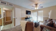 Located at 4501 Summerhill Rd in Texarkana, Texas, this single-story home offers a comfortable and well-organized layout throughout. The living room serves as the heart of the home, featuring carpet flooring, a ceiling fan with light fixture, a wall-mounted TV, and natural light streaming through blinds-covered windows. A consistent chair-rail detail runs through many rooms, adding a classic architectural touch. The galley-style kitchen is efficiently designed with warm wood cabinetry, tile flooring, a decorative mosaic backsplash, and black appliances including a refrigerator, range, and microwave. A pass-through window connects the kitchen to the adjacent dining area, which accommodates a round dining table beneath a ceiling fan and features carpet flooring. The bedrooms are generously sized with plush carpet, ceiling fans, and windows that allow ample natural light. The primary bedroom includes a charming built-in window seat, adding both character and functionality. The bathrooms feature warm wood vanities with light countertops and framed mirrors. Closet space is well-appointed, with a walk-in closet visible near the primary bath. Throughout the home, a neutral warm-beige color palette and textured ceilings create a cohesive, inviting ambiance.