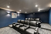 Located at 8 S Sixth St in Council Bluffs, Iowa, this private screening room is purpose-built for an immersive cinematic experience. The room is designed with a classic theater layout, featuring two tiered rows of plush black leather recliner seats, each equipped with built-in cup holders and fold-out side trays — providing both comfort and convenience for viewers. The seating arrangement ensures clear sightlines to the large flat-screen display mounted on the front wall, which serves as the room's visual centerpiece.

The interior is defined by deep navy blue walls that create a moody, theater-like ambiance, complemented by a light gray ceiling fitted with recessed can lighting. Subtle wall-mounted sconces on the rear wall add a warm accent glow, enhancing the cinematic atmosphere. The flooring throughout consists of patterned commercial-grade carpet in muted blue and gray tones, adding both comfort and acoustic quality to the space.

A decorative poster-style artwork is displayed on the rear wall, lending a stylized, venue-inspired character to the room. An illuminated exit sign and a dark-painted access door are positioned at the rear, reflecting the room's compliance with safety standards. The overall design is cohesive, functional, and purpose-driven, making this screening room an ideal private venue for film viewings or presentations.