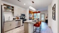 This single-floor residence is thoughtfully designed with a contemporary aesthetic, combining functional layouts with striking design details. The open-concept kitchen is a central highlight, featuring light wood-grain cabinetry extending to the ceiling, stainless steel appliances including a refrigerator, electric range, microwave, and dishwasher, and a granite-topped island with bar seating for two. Light wood-look flooring flows throughout the main living areas, enhancing the sense of openness. Pendant lighting above the island and recessed ceiling lights provide layered illumination throughout.

The living area is distinguished by a bold burnt-orange accent wall, large windows with natural light, and built-in shelving, creating a warm yet modern ambiance. The space transitions seamlessly from kitchen to living, aided by the open floor plan.

The bedrooms are carpeted for comfort, each benefiting from generous natural light through large windows dressed with blinds and curtains. One bedroom features a teal accent wall paired with a ceiling fan, while another maintains a clean, neutral palette. Both offer a calm, restful atmosphere.

The bathroom continues the granite countertop theme with a vessel-style undermount sink, wood-grain cabinetry, and a large mirror, maintaining cohesion with the rest of the home's design language.