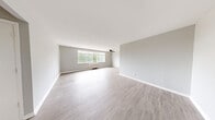 This single-floor, 3-bedroom, 2-bathroom unit offers a clean and functional layout designed for practical living. The spacious living area is a standout feature, showcasing light wood-style flooring, soft gray walls, and a large multi-pane window that invites abundant natural light and frames views of surrounding greenery. A ceiling fan adds comfort to this open and airy space.

The kitchen is efficiently designed with gray cabinetry, white countertops, and a full-size refrigerator. Upper and lower cabinets provide ample storage, while the light flooring carries through from the main living areas, maintaining a cohesive aesthetic throughout.

The generously sized primary bedroom offers a notably spacious footprint, making it well-suited as a private retreat. The additional bedrooms are bright and versatile, each featuring the same neutral tones and wood-style flooring. A dedicated closet with built-in shelving and a hanging rod provides well-organized storage.

Both bathrooms are finished with dark gray vanities, white countertops, and illuminated vanity mirrors. One bathroom features a more compact design, while the second offers a wider vanity layout with additional cabinet storage beneath. Clean white walls and matching flooring give both bathrooms a crisp, tidy appearance. A connecting hallway ties all rooms together in a cohesive and navigable floor plan.