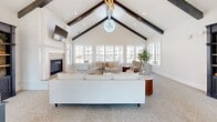 Located at 365 N Hamlin Ave in Eagle, Idaho, this single-floor space offers a thoughtfully designed open-concept layout that combines a spacious living area with a fully equipped kitchen. The architecture is immediately striking, with soaring vaulted ceilings accented by dark wood beams that run the length of the main gathering area. A statement chandelier with gold geometric detailing hangs overhead, adding a modern touch to the classic design. Large, multi-pane windows line the walls throughout, flooding the interior with abundant natural light and providing views of the surrounding community. The living room features plush neutral seating arrangements, a tile-surround fireplace with a shiplap accent wall, and soft carpet underfoot, creating a warm and inviting atmosphere. A secondary seating nook offers additional lounge space with its own generous window bank. The dining area accommodates a round table with seating for several guests. The kitchen is outfitted with dark shaker-style cabinetry, white quartz countertops, a textured mosaic tile backsplash, stainless steel appliances, and warm hardwood flooring. A pool table in the recreation zone rounds out this versatile, well-appointed community gathering space.