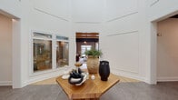 Located at 6132 Mallet Dr in Raleigh, NC, this single-floor clubhouse is a thoughtfully designed community amenity space that blends modern elegance with eclectic character. The grand entry foyer immediately sets the tone, boasting soaring double-height ceilings clad in crisp white paneling, large windows that flood the space with natural light, and a striking octagonal wood table as a central focal point adorned with curated decorative accents.

From the foyer, the space opens into expansive lounge and social areas featuring warm hardwood flooring throughout. Exposed brick accent walls, dark-painted ceiling beams, and an open shelving unit lend an industrial-chic aesthetic to the main gathering room, which includes a tufted leather sofa, woven accent chairs, a linear fireplace, and built-in bench seating alongside wall-mounted displays.

The kitchenette is well-appointed with stainless steel appliances, a subway tile backsplash, dark countertops, light gray cabinetry, a statement range hood, and industrial-style wall sconces. A dedicated business center provides workstations equipped with computers and a shared printer, finished with textured wallcovering for a polished, functional environment. The overall ambiance balances comfort, utility, and design sophistication.
