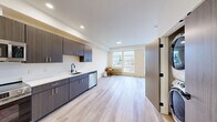 Located at 3909 N Wall St in Spokane, WA, this well-designed one-bedroom, one-bathroom unit offers a thoughtfully planned layout with contemporary finishes throughout. Light-toned hardwood-style flooring runs continuously across the entire space, creating a cohesive and clean aesthetic.

The kitchen is a standout feature, equipped with full stainless steel appliances including a refrigerator, range, built-in microwave, and dishwasher. Dark wood-grain cabinetry with sleek hardware lines the walls, complemented by crisp white countertops and a matte black sink fixture, striking a bold modern contrast.

The open living area flows naturally from the kitchen and is bathed in natural light from large windows that frame views of the surrounding Spokane neighborhood. The bedroom is generously proportioned, featuring its own large window with additional neighborhood views, a ceiling fan, and a sliding door closet with built-in shelving.

The bathroom maintains the same modern design language, with wood-toned cabinetry, a white countertop vanity, a large round mirror with a black frame, and light tile flooring. Matte black hardware accents throughout the unit tie the design together cohesively. The overall ambiance is clean, bright, and contemporary, ideal for those seeking a modern living space in Spokane.