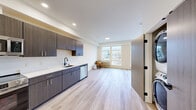 Located at 3909 N Wall St in Spokane, WA, this well-designed one-bedroom, one-bathroom unit offers a thoughtfully planned layout with contemporary finishes throughout. Light-toned hardwood-style flooring runs continuously across the entire space, creating a cohesive and clean aesthetic.

The kitchen is a standout feature, equipped with full stainless steel appliances including a refrigerator, range, built-in microwave, and dishwasher. Dark wood-grain cabinetry with sleek hardware lines the walls, complemented by crisp white countertops and a matte black sink fixture, striking a bold modern contrast.

The open living area flows naturally from the kitchen and is bathed in natural light from large windows that frame views of the surrounding Spokane neighborhood. The bedroom is generously proportioned, featuring its own large window with additional neighborhood views, a ceiling fan, and a sliding door closet with built-in shelving.

The bathroom maintains the same modern design language, with wood-toned cabinetry, a white countertop vanity, a large round mirror with a black frame, and light tile flooring. Matte black hardware accents throughout the unit tie the design together cohesively. The overall ambiance is clean, bright, and contemporary, ideal for those seeking a modern living space in Spokane.