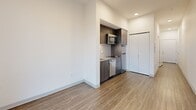 Located at 5230 39th Ave S in Seattle's Hillman City neighborhood, this efficiently designed studio unit makes smart use of its compact footprint across a single floor. The open-concept layout seamlessly combines the living, dining, and kitchen areas into one cohesive space, creating a functional and uncluttered environment. The kitchenette is outfitted with dark wood cabinetry, a microwave, a compact dishwasher, and a sink, all framed by a classic subway tile backsplash. Wood-look flooring runs throughout the unit, lending warmth and visual continuity across every room. A large picture window in the main living area floods the space with natural light and offers pleasant views of the surrounding Seattle neighborhood, including tree canopy and rooftops. Crisp white walls and clean-lined finishes give the unit a modern, minimalist aesthetic. The full bathroom features a soaking tub with overhead shower, a wall-mounted vanity with dark wood cabinetry and a white countertop, and matching wood-look tile flooring. A dedicated closet provides generous built-in storage, and in-unit laundry adds a layer of everyday convenience. The overall design is clean, contemporary, and well-suited for efficient urban living.