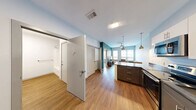 This modern one-bedroom, one-bathroom unit at 919 E Genesee Street in Syracuse, New York offers a well-designed, efficient layout across a single floor. The contemporary kitchen is equipped with stainless steel appliances — including a full-size refrigerator, range, microwave, and dishwasher — complemented by dark lower cabinetry, white upper cabinets, and dark granite-style countertops. Warm hardwood-style flooring runs throughout the main living areas, enhancing the clean, modern aesthetic. The living room is bright and open, featuring two large windows with horizontal blinds that invite natural light and provide views of the surrounding neighborhood. The bedroom is a comfortable, carpeted space with its own window offering additional natural light and an urban outlook. A dedicated workspace area within the bedroom adds functional versatility. The full bathroom features a soaking tub with shower, a dark-cabinet vanity, and matching hardwood-style flooring consistent with the rest of the unit. A closet provides additional storage. The unit's entry door features a keypad access system, adding a layer of modern security. Clean white walls and a neutral palette throughout give the space a fresh, contemporary feel well-suited for urban living in Syracuse.