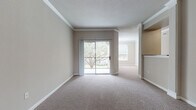 This single-floor residence offers a thoughtfully designed layout that balances comfort and functionality throughout. The main living area is finished with plush wall-to-wall carpeting, neutral warm-toned walls, and elegant crown molding, creating a welcoming atmosphere. A sliding glass door opens to a private outdoor area, allowing natural light to pour in and offering views of mature trees. Crown molding and textured ceilings add a refined architectural touch to the living space, which flows openly into an adjacent room.

The kitchen is well-equipped with rich dark wood cabinetry, dark granite countertops, a stainless steel sink, and black appliances, all set atop warm hardwood-style flooring that extends through the utility areas. A dedicated laundry room with full-size washer and dryer hookups provides added convenience.

The bedrooms are generously sized with soft carpeting, ample natural light from large windows with views of surrounding greenery, and ceiling fans for comfort. The bathrooms feature dark wood vanities with dual sinks, white countertops, large mirrors, and hardwood-style flooring. A carpeted staircase with a polished wood handrail connects levels within the building. Overall, the space presents a clean, neutral palette suited for a variety of living styles.