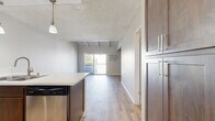 Located at 9901 Lurline Ave in the Chatsworth neighborhood of Los Angeles, this thoughtfully designed unit makes efficient use of its single-floor layout. The open-concept kitchen and living area serve as the heart of the space, seamlessly connecting day-to-day living and dining functions. The kitchen is outfitted with rich dark-wood cabinetry, a light quartz countertop peninsula with an undermount double sink, stainless steel appliances including a refrigerator, range, microwave, and dishwasher, and elegant pendant lighting overhead. Light wood-style flooring extends throughout, contributing to a cohesive, modern aesthetic. The living area is distinguished by vaulted ceilings with exposed white-painted wood beams, lending architectural character and an airy sense of height. A sliding glass door opens onto a private balcony, framing views of lush palm trees and the landscaped courtyard below. Two bathrooms round out the layout — one featuring dark-framed frosted glass sliding closet doors, wood-finish cabinetry, and a sleek vanity, while the second offers a clean, all-white tub-shower combination. A wall-mounted AC unit ensures year-round comfort. The overall ambiance is fresh, modern, and move-in ready.