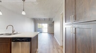 Located at 9901 Lurline Ave in the Chatsworth neighborhood of Los Angeles, this thoughtfully designed unit makes efficient use of its single-floor layout. The open-concept kitchen and living area serve as the heart of the space, seamlessly connecting day-to-day living and dining functions. The kitchen is outfitted with rich dark-wood cabinetry, a light quartz countertop peninsula with an undermount double sink, stainless steel appliances including a refrigerator, range, microwave, and dishwasher, and elegant pendant lighting overhead. Light wood-style flooring extends throughout, contributing to a cohesive, modern aesthetic. The living area is distinguished by vaulted ceilings with exposed white-painted wood beams, lending architectural character and an airy sense of height. A sliding glass door opens onto a private balcony, framing views of lush palm trees and the landscaped courtyard below. Two bathrooms round out the layout — one featuring dark-framed frosted glass sliding closet doors, wood-finish cabinetry, and a sleek vanity, while the second offers a clean, all-white tub-shower combination. A wall-mounted AC unit ensures year-round comfort. The overall ambiance is fresh, modern, and move-in ready.