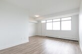 Located at 1 Rosemount Dr in Toronto's Scarborough area, this 1-bedroom, 1-bathroom unit offers a clean, modern aesthetic with a thoughtfully organized layout across a single floor. Light wood-look flooring runs throughout the space, complementing the crisp white walls and creating a bright, cohesive feel.

The open living area is a standout feature, highlighted by a wide bank of floor-to-ceiling windows that flood the room with natural light and offer sweeping views of the surrounding cityscape. A baseboard heating system runs along the window wall, ensuring year-round comfort.

The kitchen is efficiently designed in a galley style, featuring white shaker cabinetry extending to the ceiling for ample storage, a grey countertop with a double stainless steel sink, white subway tile backsplash, and stainless steel appliances including a refrigerator, electric range, and over-the-range microwave.

The bedroom is a comfortable, well-proportioned room with its own window offering city views, baseboard heating, and a set of sliding panel closet doors providing generous storage. The full bathroom is finished in a clean, contemporary style with white subway tile surrounding the shower-tub combo, a single vanity with white cabinetry, and a large mirror. A hallway connects all areas of the unit, completing this practical and attractive urban residence.