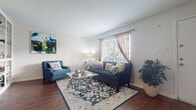Located at 8000 W Tidwell Rd in Houston, Texas, this single-floor residence offers a thoughtfully laid-out living space with a warm and inviting atmosphere throughout. The living room serves as the heart of the home, featuring rich hardwood-style flooring, neutral white walls, and natural light streaming in through windows dressed with blinds and sheer curtains. A built-in shelving unit adds both function and character to the space.

The galley-style kitchen is efficiently designed with white cabinetry, white countertops, and a dark tile backsplash that adds contrast. Black appliances, including a refrigerator, electric range, and dishwasher, are neatly integrated alongside a double sink, maximizing the use of the available space.

The bedroom is a serene retreat, carpeted for comfort, with a window that allows natural light and outdoor views. It connects to a spacious walk-in closet complete with built-in shelving and hanging rods, offering generous storage.

The bathroom features a wide vanity with a single sink, white cabinetry, and a large mirror with louvered cabinet doors. The layout separates the vanity area from the toilet and storage space, enhancing functionality. Consistent carpeting and clean finishes carry through, creating a cohesive and comfortable living environment throughout the home.