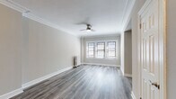 Located on West Fullerton Parkway in Chicago's desirable Lincoln Park neighborhood, this thoughtfully renovated single-floor residence blends classic architectural details with modern updates throughout. Hardwood-style plank flooring flows continuously across all rooms, complemented by crisp white crown molding and baseboards that lend an elegant, traditional character to the space.

The generously proportioned living area features a ceiling fan, ornate crown molding, and a triple window arrangement that draws in abundant natural light. A separate bedroom offers corner windows on two walls, providing cross-ventilation and a bright, airy feel, also equipped with a ceiling fan overhead.

The compact kitchen is efficiently designed with white Shaker-style cabinetry, a stainless steel refrigerator and gas range, and a cool-toned subway tile backsplash that adds a stylish accent. Warm flush-mount lighting and decorative crown molding detail the transition area between the living and kitchen spaces.

The bathroom is a standout feature, showcasing a deep soaking tub with an overhead shower fixture, a sleek gray vanity with modern hardware, wood-look flooring, and a charming cast-iron radiator—a nod to the building's historic character. Built-in shelving provides convenient storage within the bathroom as well. Classic cast-iron radiators are found throughout, further reflecting the home's enduring architectural heritage.