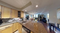 This single-floor residence is thoughtfully designed with an open-concept layout that seamlessly connects the kitchen, dining, and living areas. The kitchen is outfitted with warm maple cabinetry, dark granite countertops, a mosaic tile backsplash, and stainless steel appliances including a range, built-in microwave, and a double-basin sink set into a peninsula that doubles as a breakfast bar. Recessed and track lighting illuminate the space effectively throughout.

The living area features rich, dark hardwood flooring that extends through the main living spaces and bedrooms. Large windows dressed with vertical blinds and drapery panels allow natural light to fill the room, creating a bright and welcoming atmosphere. The space comfortably accommodates a full seating arrangement.

The bedrooms continue the hardwood flooring and offer generous window coverage, providing natural light and exterior views. The bathroom includes maple vanity cabinetry with a stone-topped countertop, an undermount sink, a large mirror with overhead lighting, and tile flooring. A hallway connects the private areas of the residence, maintaining a clear and functional flow throughout the home.