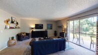 Located at 8024 Southside Blvd in Jacksonville, FL, this single-floor residence offers a well-organized layout with distinct living spaces designed for everyday comfort. The expansive living room serves as the heart of the home, featuring plush carpeting, textured ceilings, decorative wall shelving, and a sliding glass door that floods the room with natural light and provides views of the surrounding greenery. The space comfortably accommodates generous seating arrangements, making it ideal for relaxing or entertaining. Adjacent to the living room, the dining area features dark hardwood-style flooring, a stylish pendant light fixture centered above a round glass dining table, and a window that brings in additional natural light. The galley-style kitchen is equipped with white cabinetry, granite-look countertops, a stainless steel sink, and white appliances, all set atop dark hardwood-style flooring. The bedrooms are carpeted and well-proportioned, each featuring windows that allow natural light to filter through. The full bathroom includes a shower-tub combination, dark hardwood-style flooring, and clean, neutral finishes. Throughout the home, a cohesive neutral color palette and thoughtful design details contribute to a warm, inviting ambiance.